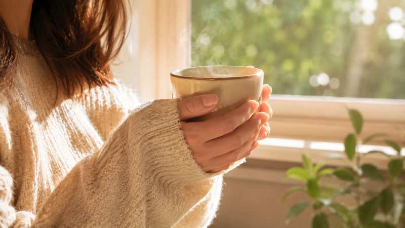 窓辺で温かい飲み物を手に、ほっと一息ついてリラックスする様子